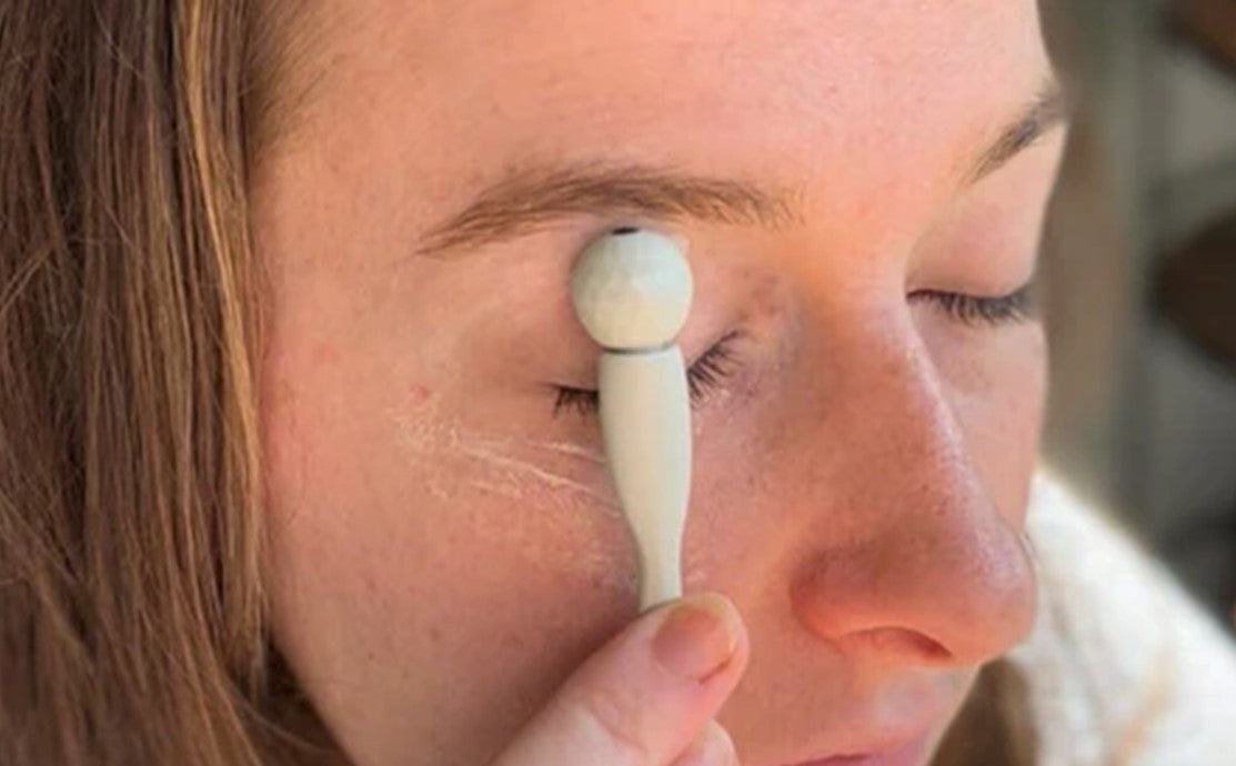 Woman using a cooling under eye roller beneath her eye to reduce the look of puffiness and dark circles