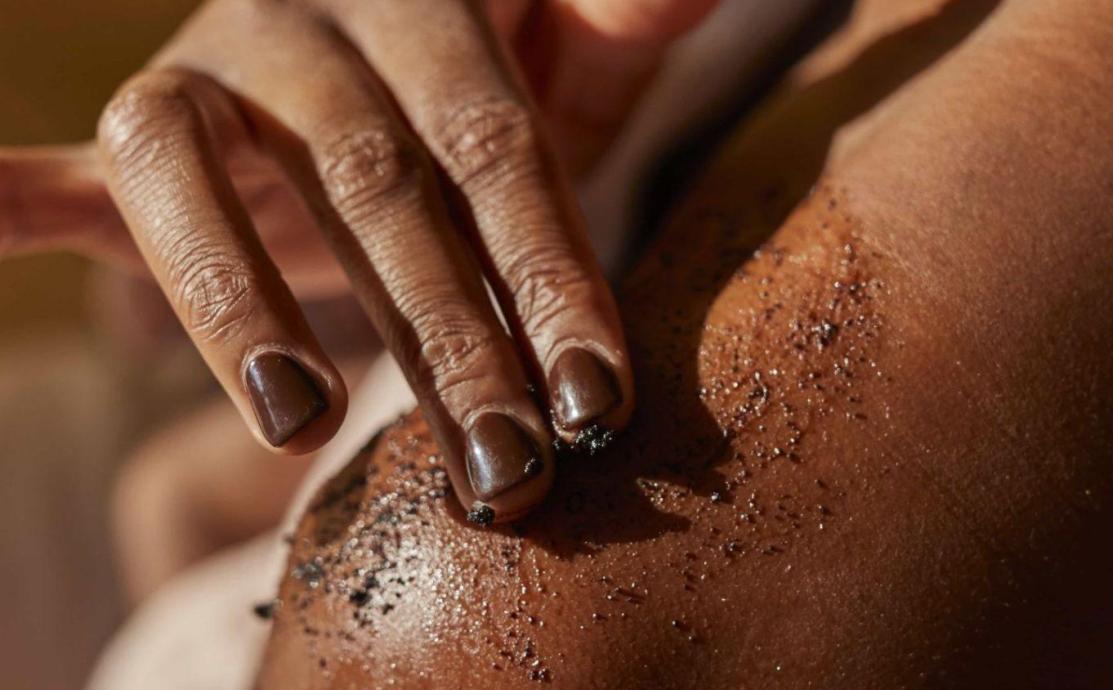 Hands massaging upcycled coffee body scrub into a shoulder, showing how often to exfoliate with a body scrub compared with a face scrub