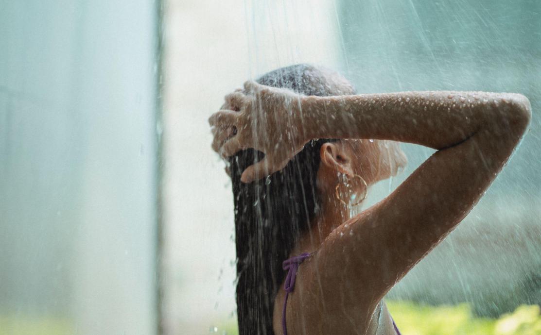 Woman washing her hair under a shower, rinsing shampoo from an itchy scalp as part of a gentle autumn scalp care routine