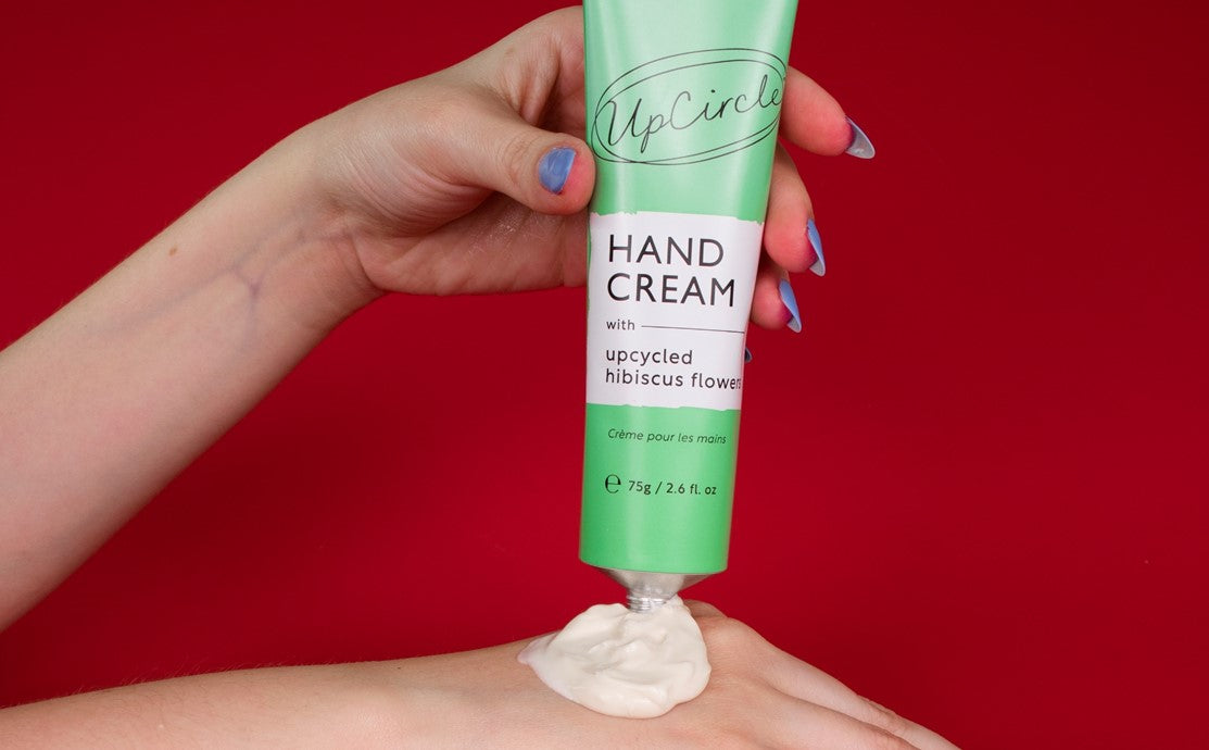 Hand dispensing sustainable face moisturiser from an UpCircle tube onto a palm against a deep red background, illustrating what makes a moisturiser sustainable